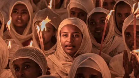 AFP Orthodox Christian women wearing white head scarves and holding candles at prayers ahead of Christmas celebrations at the Bole Medhanialem Church in Addis Ababa - 6 January 2024