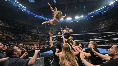 Getty Images Women's world champion Tiffany Stratton flying through the air against Charlotte Flair, with security looking on shocked