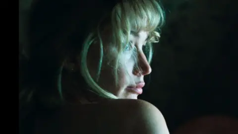 Okasha Jennifer Lawrence's face and one bare shoulder lit against a dark background in a still from Die My Love