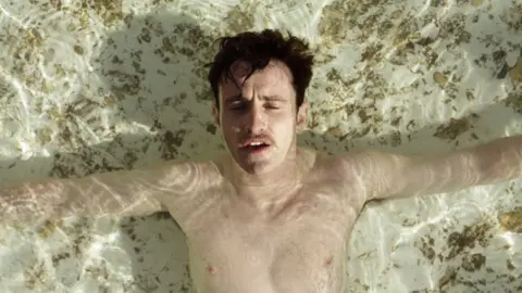 Fair Winter LLC Paul Mescal with his arms out, seen from above in shallow water