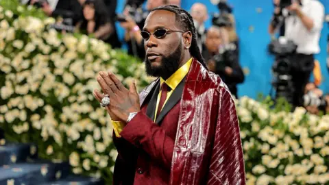 Getty Images Burna Boy poses on the Met Gala red carpet, wearing the suit and cape Ozwald Boateng made for him