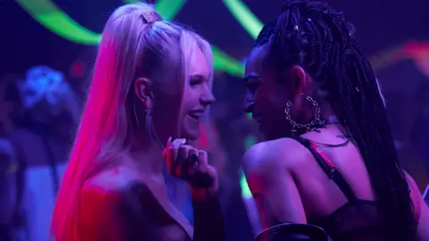 BBC/Hera/Enda Bowe Sasha (Hannah Jones) and Sticky Nikki (Alex Thomas-Smith) in a nightclub, chatting and laughing.