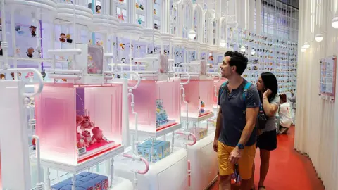 Getty Images A man and a woman, look amazed, in front of a wall of Pop Mart dolls