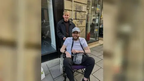 Supplied Stephen Jefferson and his brother-in-law Daniel Swales smiling at the camera. Mr Jefferson has blonde hair is dressed in black trousers, jacket and t-shirt. Mr Swales has a cap on and is wearing black trousers, a white t-shirt and a grey cross body bag.