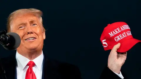 Getty Images US President Donald Trump holding a red baseball cap with the slogan Make America Great Again on it