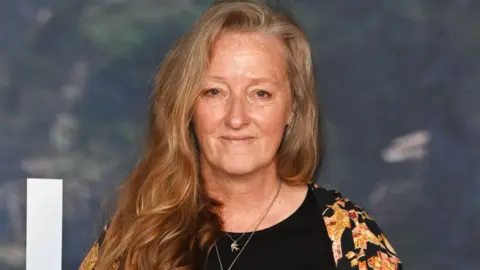 Getty Images Raynor Winn attends the UK Special Screening of The Salt Path at The Curzon Soho on 22 May 2025 in London. She has long strawberry blonde hair and is wearing a black and yellow top.