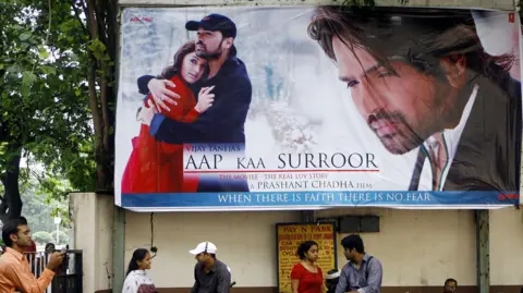 AFP via Getty Images Couples stand under a hoarding advertising Bollywood box-office hit movie "Aap Kaa Surroor" (Your intoxication) in Mumbai, 07 July 2007. 
