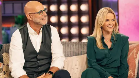 Getty Images (l-r) Harlan Coben in a white shirt, Reese Witherspoon in a green trouser suit