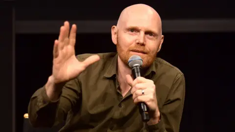 Getty Images Bill Burr in a khaki shirt, speaking into a mic