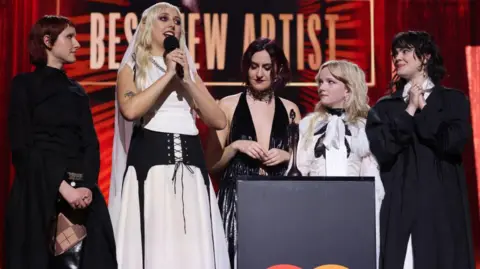 Getty Images Georgia Davies of The Last Dinner Party gives an acceptance speech at the 2025 Brit Awards while her bandmates look on