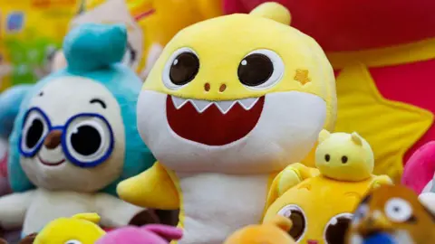 Getty Images A row of Pinkfong's Baby Shark character soft toys on a display. The main yellow Baby Shark sits at the centre.