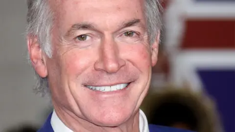 Getty Images A close-up of a man with silver hair who is smiling at the camera.