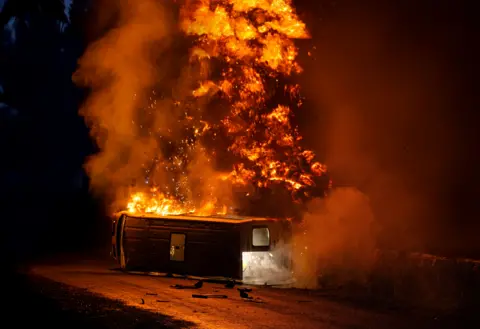 ITV A coach on its side on fire, with huge flames rising into the night sky, in a scene from Corriedale